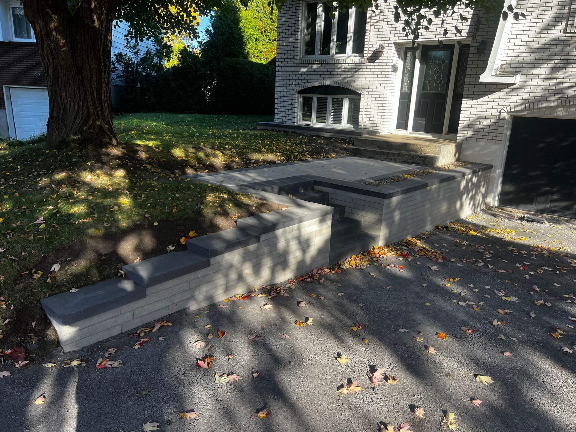 Marches et rampe en béton menant à l'entrée d'une maison en pierre, allée au premier plan.