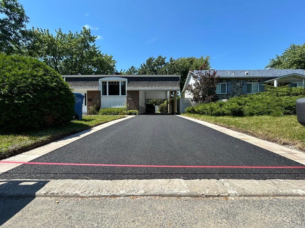 Allée asphaltée nouvellement pavée menant à une maison avec un abri d'auto attenant, située par une journée ensoleillée.