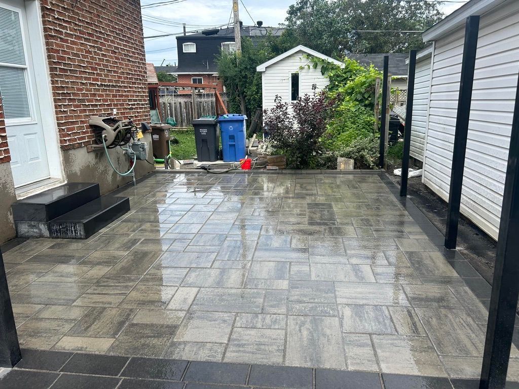 Terrasse en briques avec pavés en pierre et bordure noire. Jardin avec cabanons, marches et poubelles.