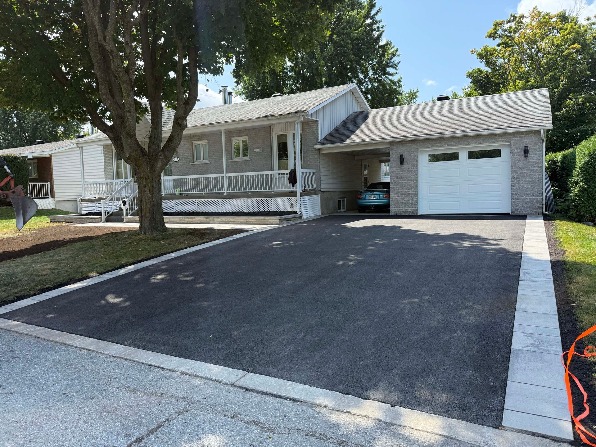 Maison avec allée asphaltée, garage attenant et une voiture stationnée à l'intérieur.