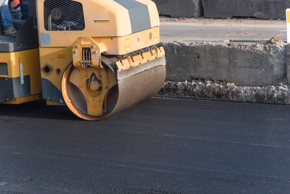 Un rouleau jaune et gris déroule l'asphalte sur une route.