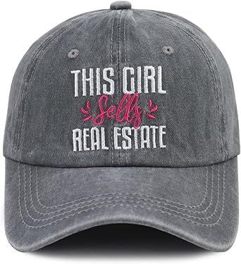 Gray cap with white text “THIS GIRL sells REAL ESTATE” and pink script “sells” on the front