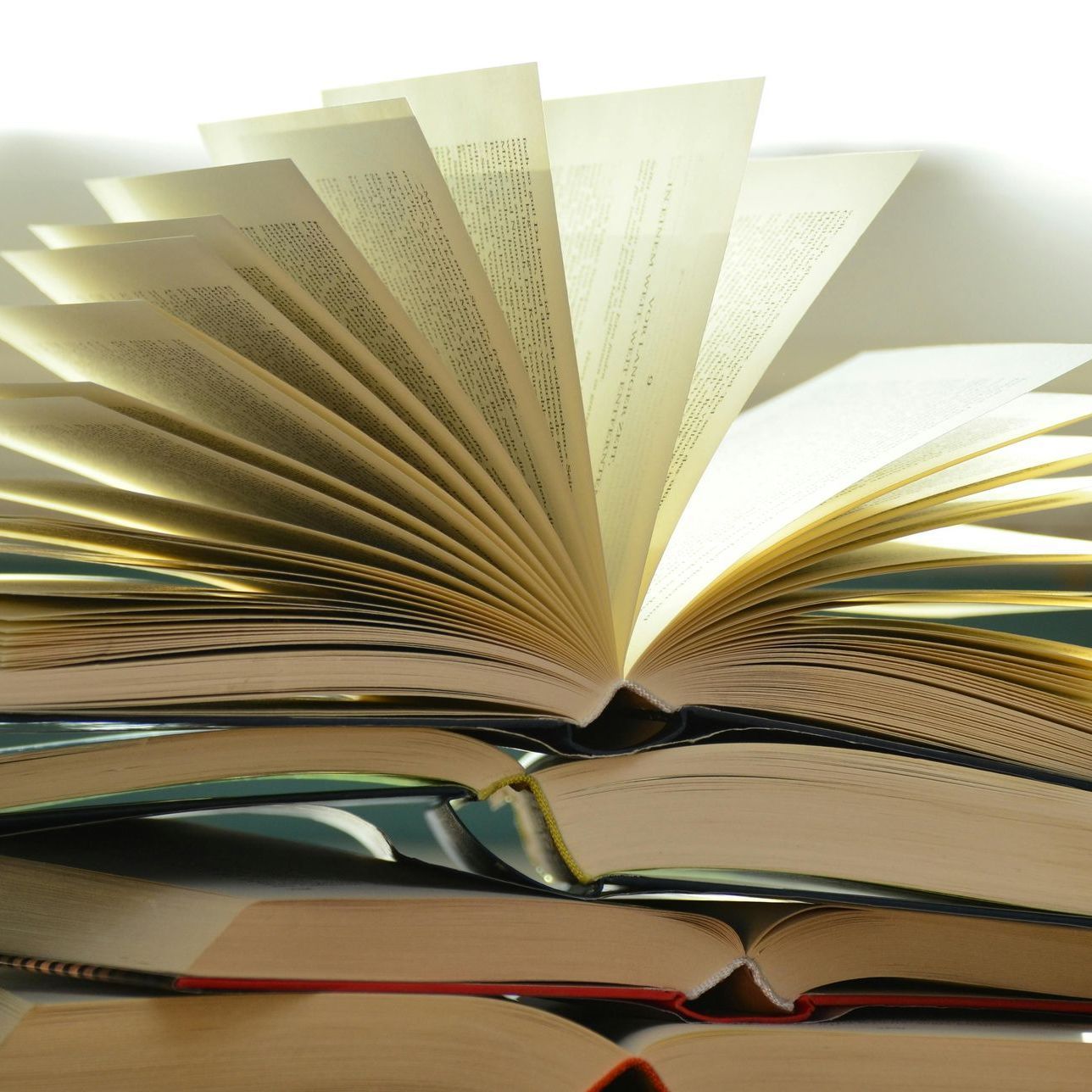 Stack of open books with pages fanned out in warm light