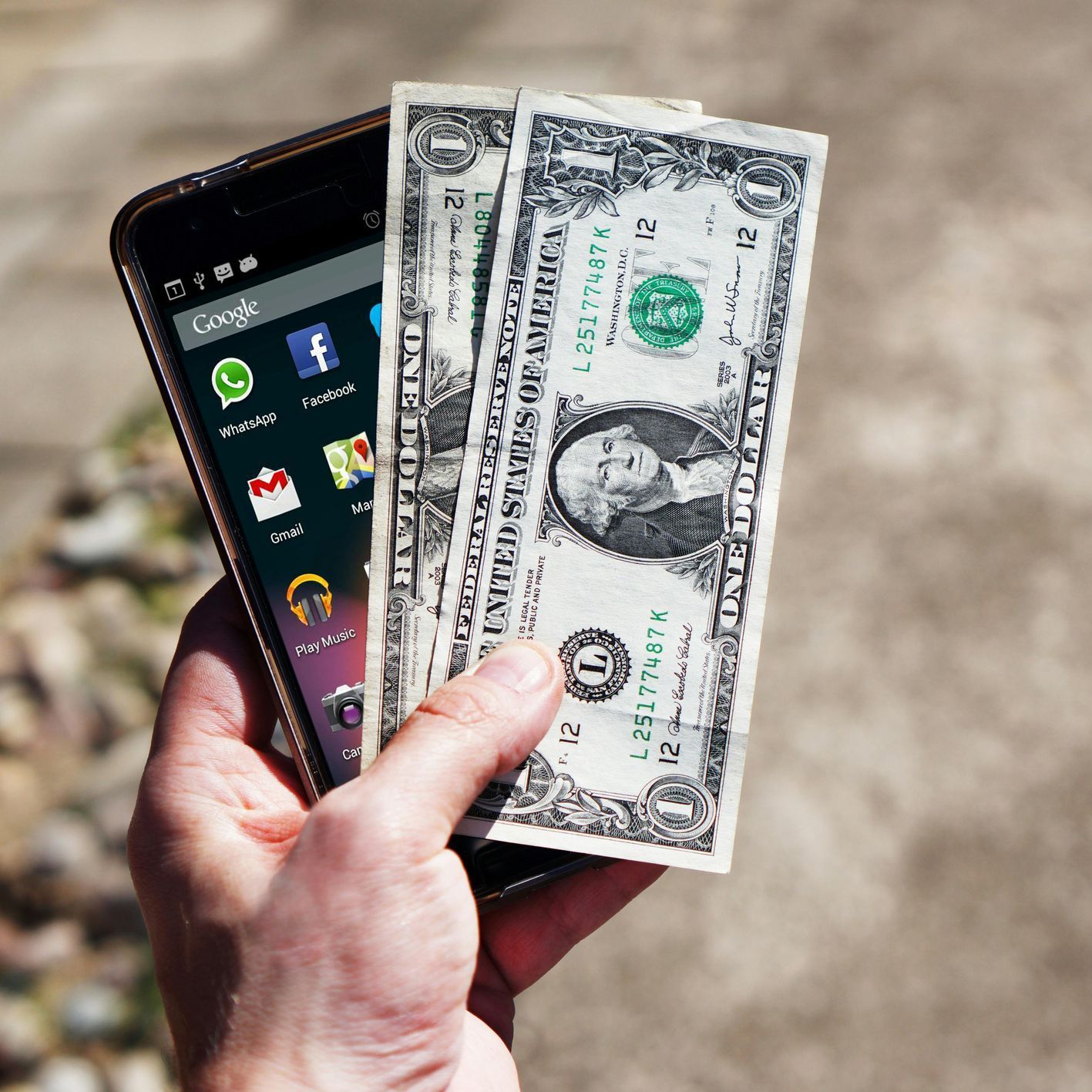 Hand holding a smartphone with cash and a one-dollar bill fanned in front