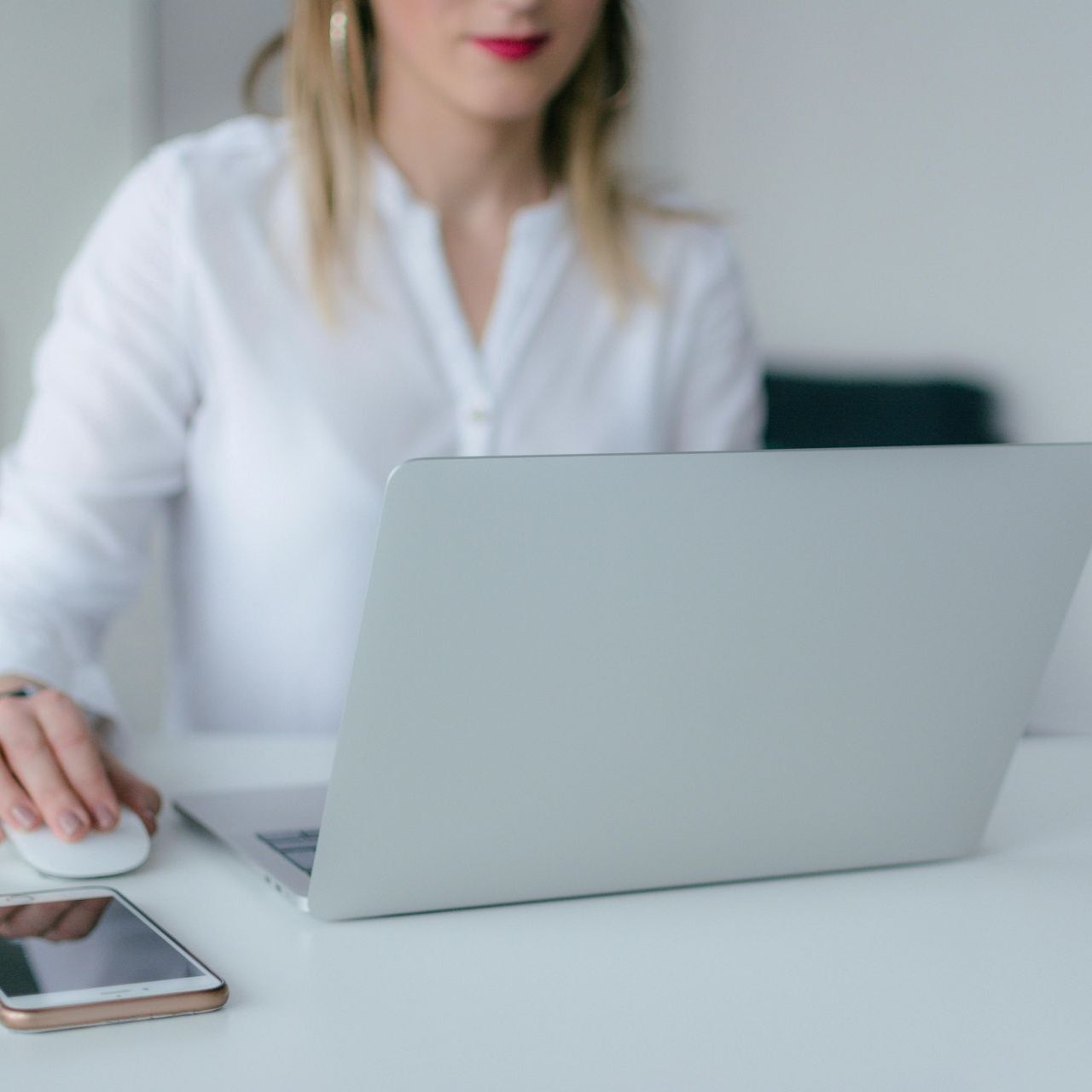 Person using a laptop at a desk with a smartphone nearby in a bright office setting