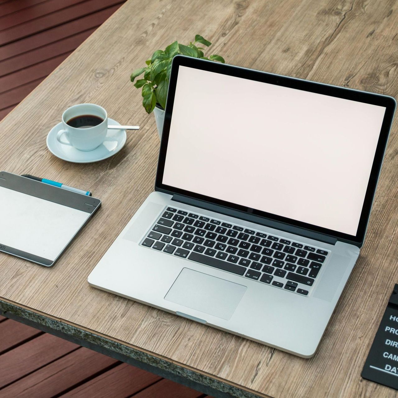 Laptop on a wooden table beside a coffee cup and notepad, with a blank screen.