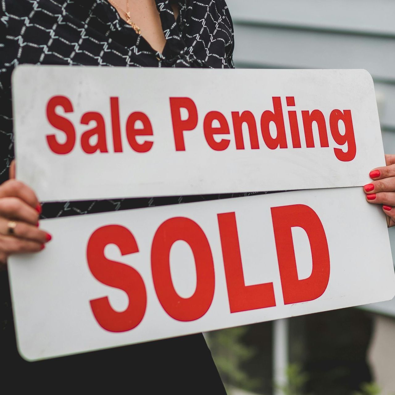 Person holding a white real estate sign with red text: “Sale Pending” and “SOLD.”