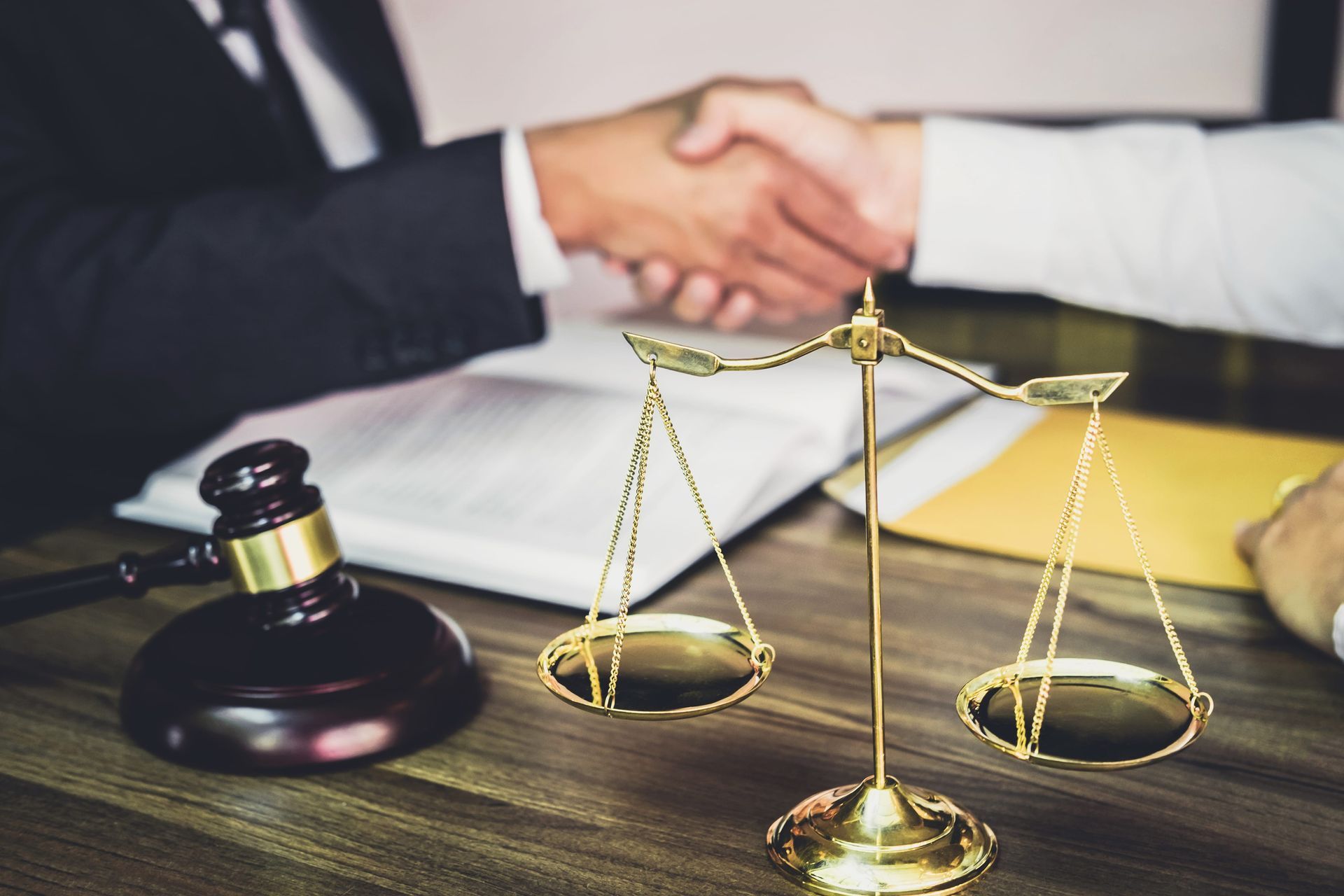 Handshake beside legal gavel and scales of justice on a desk, symbolizing a business agreement