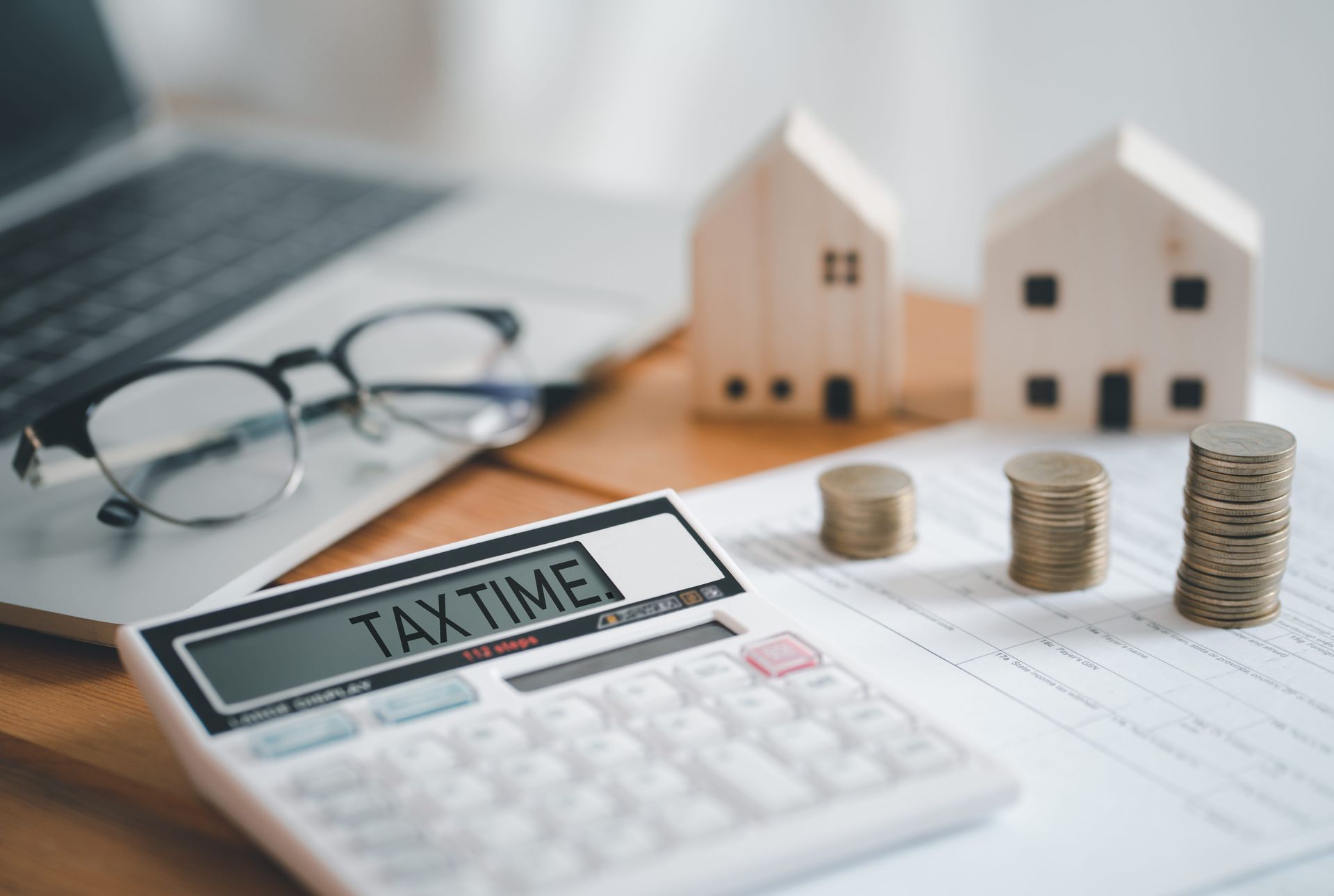 Tax time workspace with calculator, glasses, house models, and stacked coins on paperwork