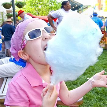 A little girl wearing sunglasses is eating cotton candy