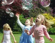 Three little girls are playing with soap bubbles in a park.