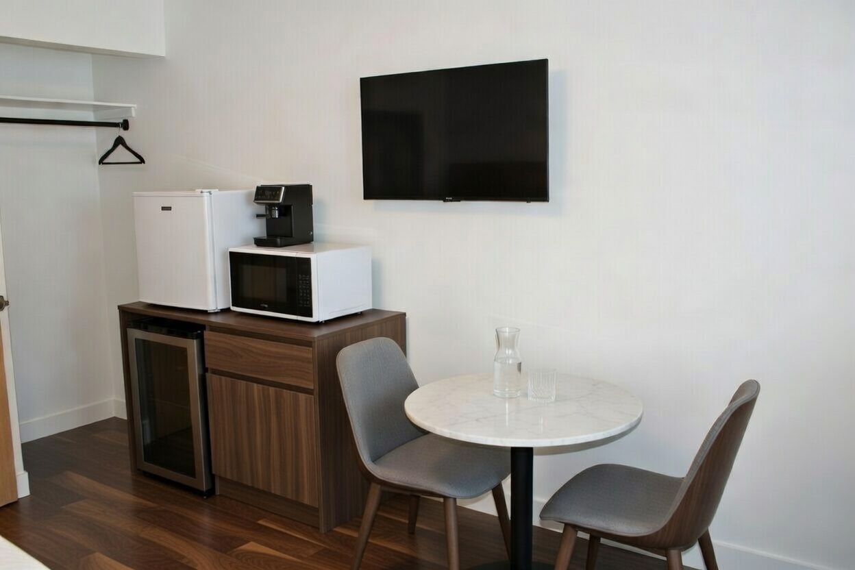 Compact kitchenette with mini fridge, microwave, wall TV, and a small round table with two chairs.