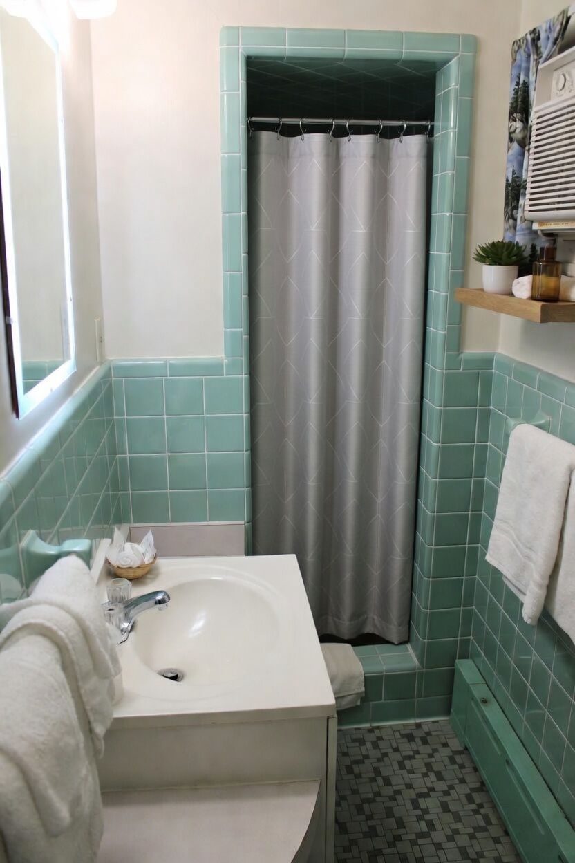 Small mint-green bathroom with sink, shower curtain, towel rack, and window ledge.