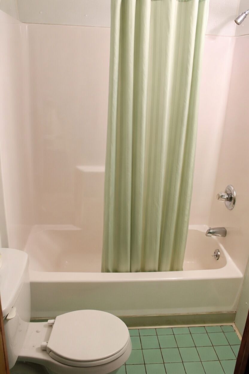 Small bathroom with a white tub, pale green shower curtain, and green tiled floor.