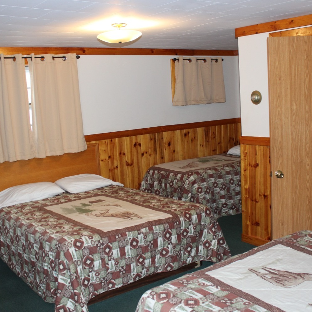 Small hotel room with three beds, wood-paneled walls, curtains, and ceiling light
