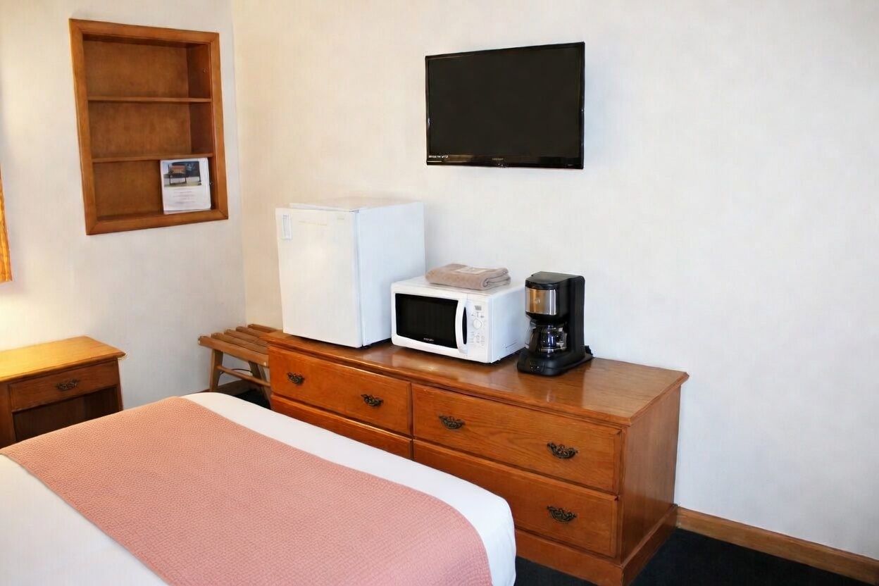 Hotel room with bed, dresser, wall TV, mini-fridge, microwave, and coffee maker