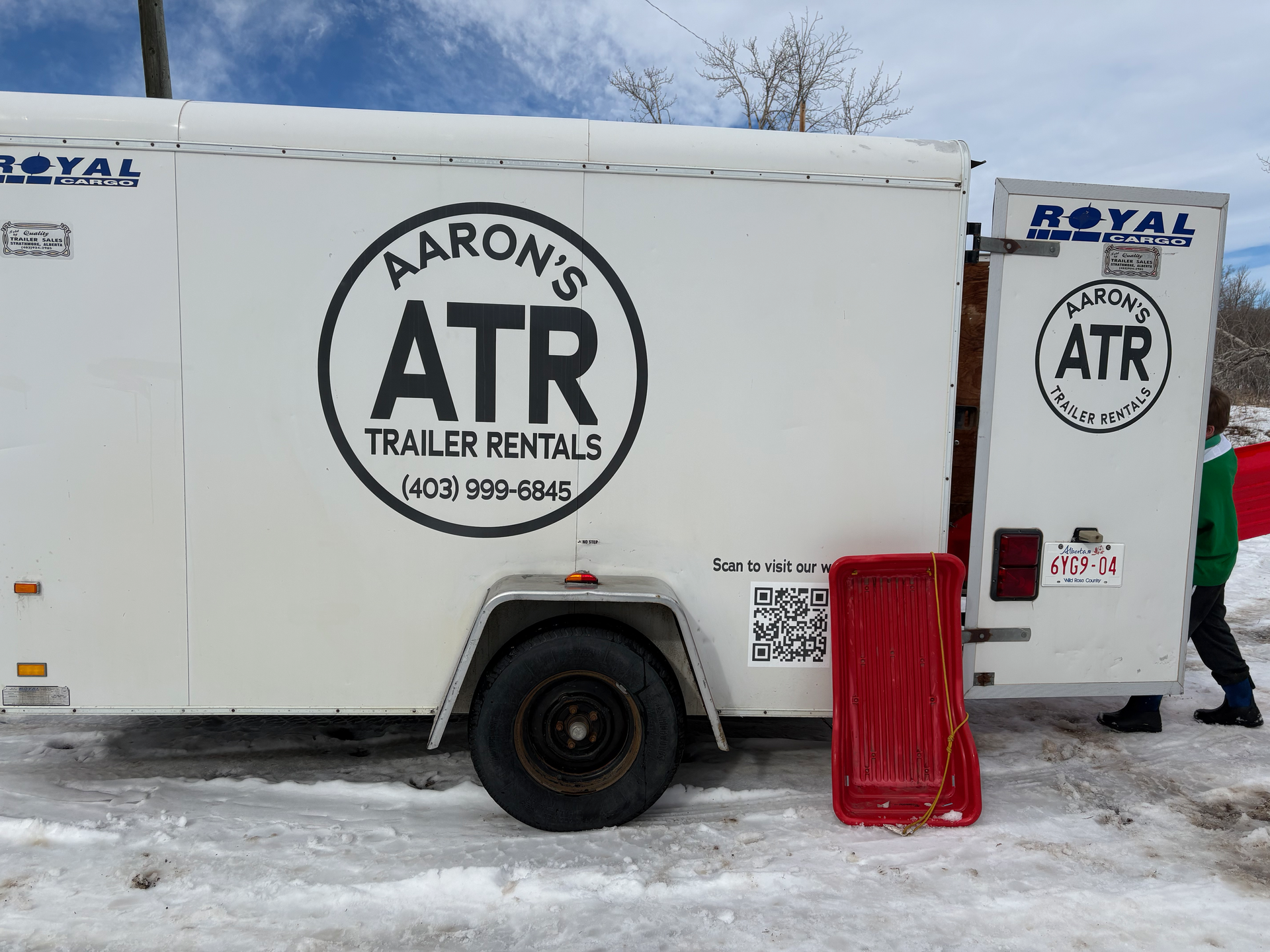 Black enclosed trailer with double wheels and side door, parked in snowy area.