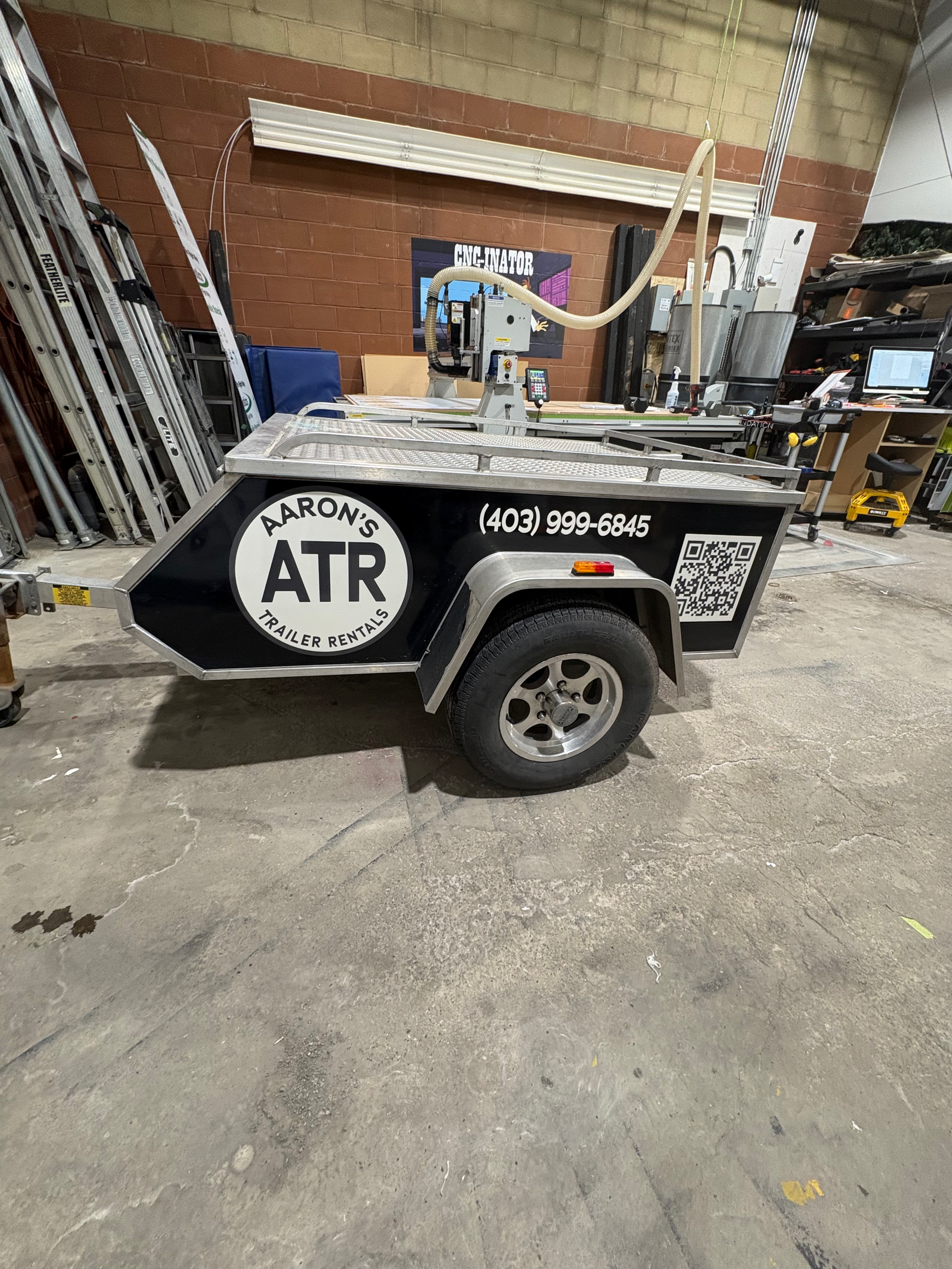 Open aluminum utility trailer with a black exterior; car is in the background.