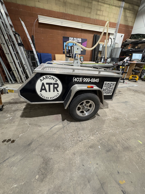 Open aluminum utility trailer with a black exterior; car is in the background.