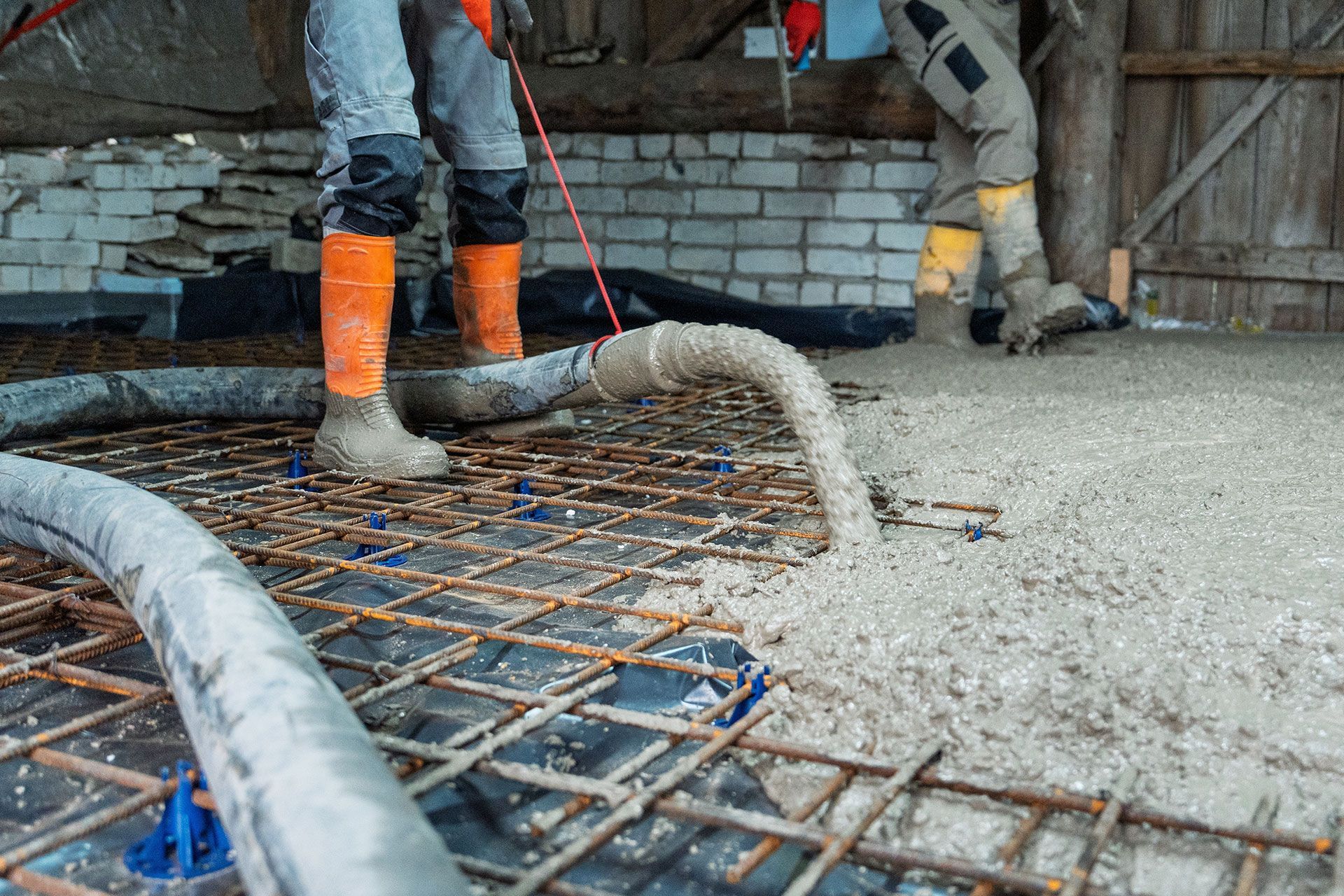 Workers pouring concrete over rebar at a construction site, with a hose in the foreground.