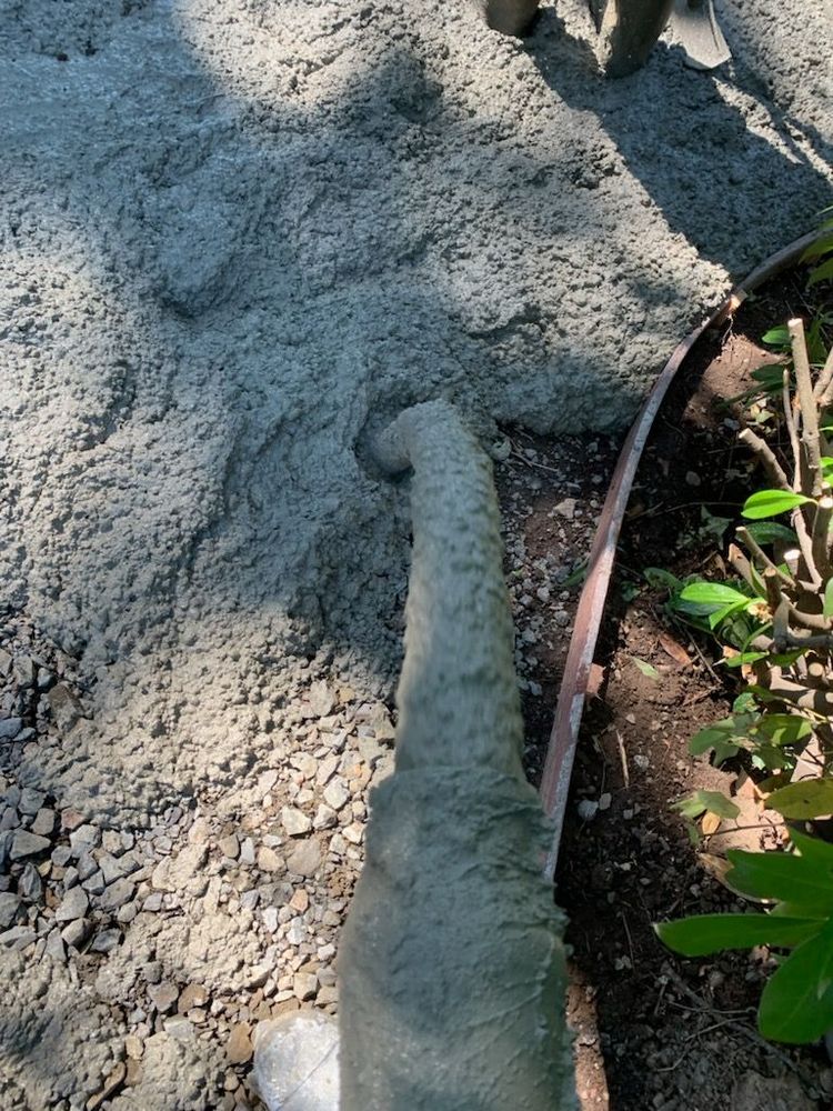 A concrete walkway edge beside rough gray gravel and small green plants, with a rust-colored border line.