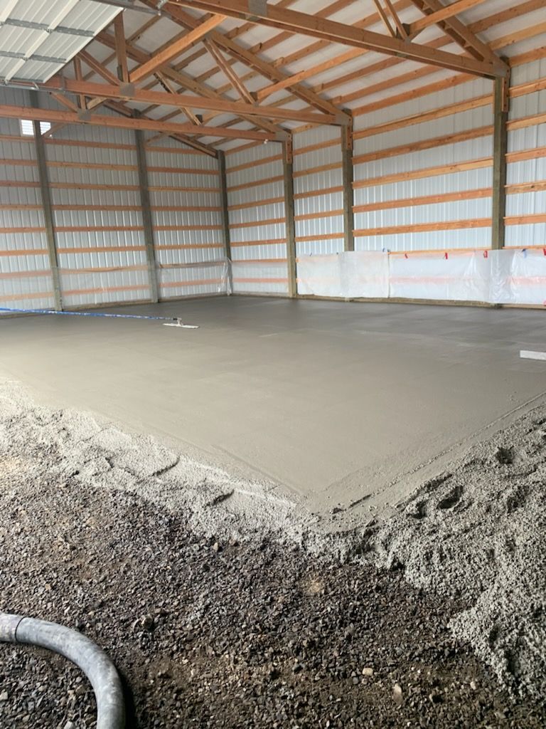 Workers pouring concrete floor between wooden forms while wearing boots and gloves