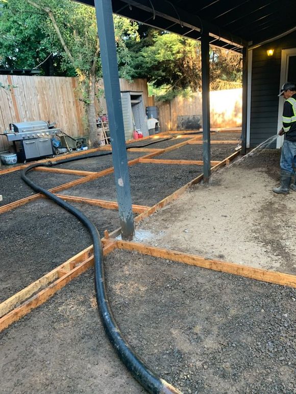 A concrete walkway edge beside rough gray gravel and small green plants, with a rust-colored border line.