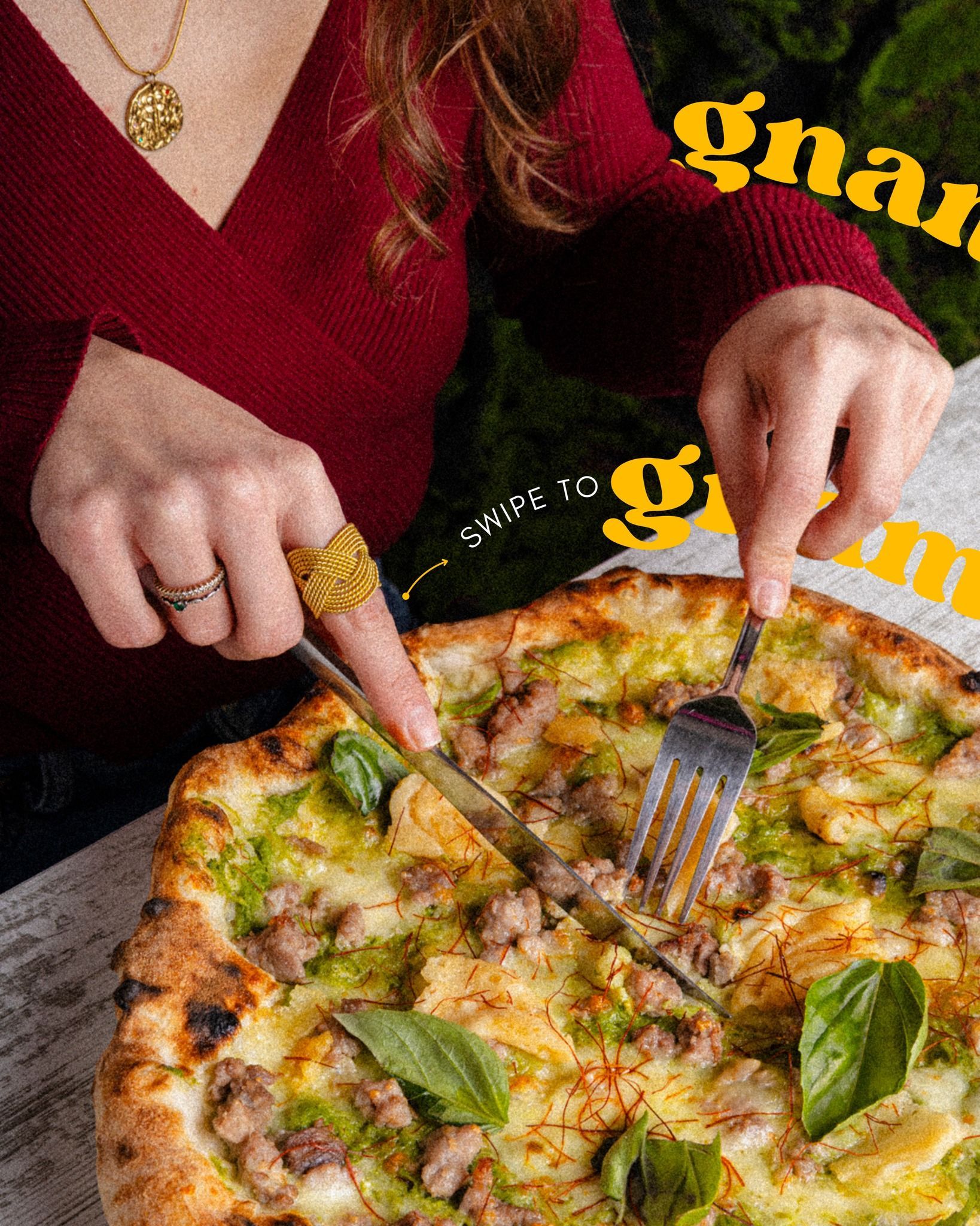 Donna che taglia la pizza con coltello e forchetta, indossando un maglione bordeaux.