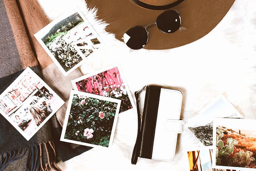 Flat lay of Polaroid photos, a smartphone, sunglasses, and a notebook on a white desk