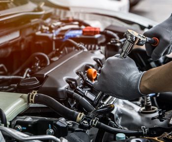 A man is working on the engine of a car with a wrench.
