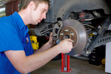 A man in a blue shirt is working on a car in a garage.