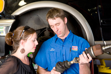 A man and a woman are looking at a driveshaft in a garage.