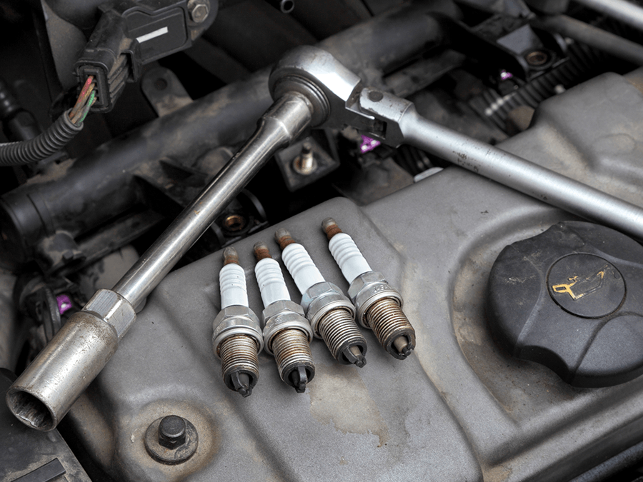 A close up of a car engine with spark plugs and a wrench.