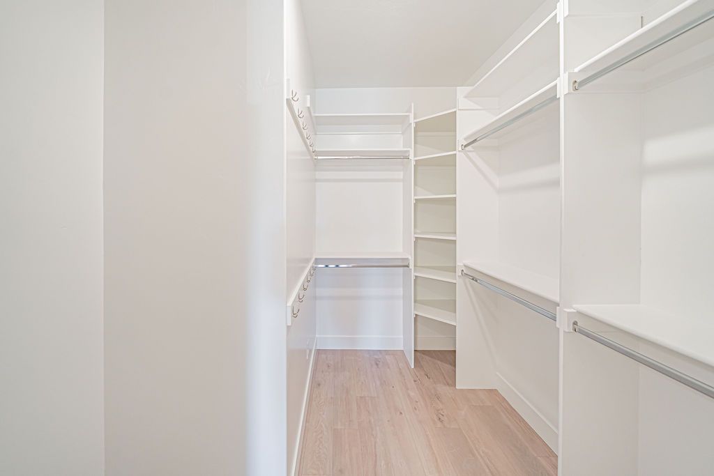 Empty white walk-in closet with shelves and hanging rods. Light wood floors.