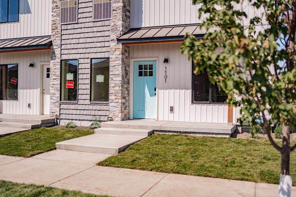 Row of townhomes with light blue front door, stone and white siding, and green grass.