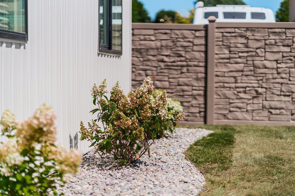 White house exterior with stone fence and small garden with bushes and rocks.