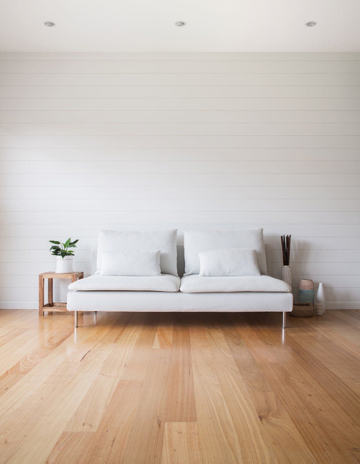 White sofa against a white slatted wall, hardwood floor, small plant on a wooden side table.