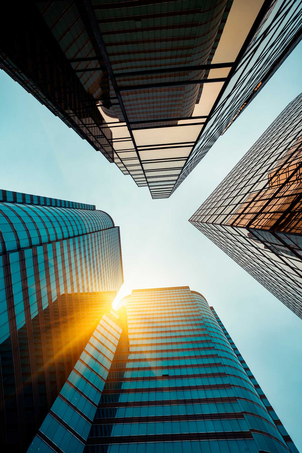 Skyscrapers, shot from below, angled toward each other with the sun shining between them.