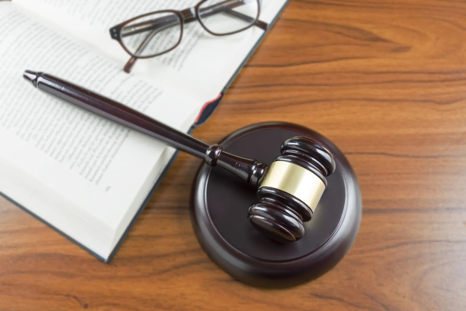 Gavel on wooden block with an open book and eyeglasses; legal and justice concept.