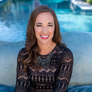 Smiling woman in a black lace top seated by a pool on a blue cushion