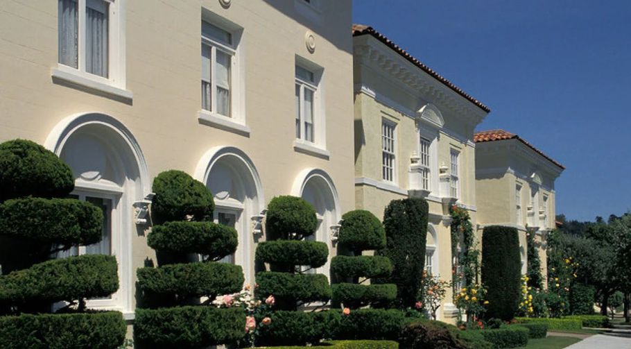 Trimmed shrubs in front of cream-colored townhouses with arched windows and red roofs