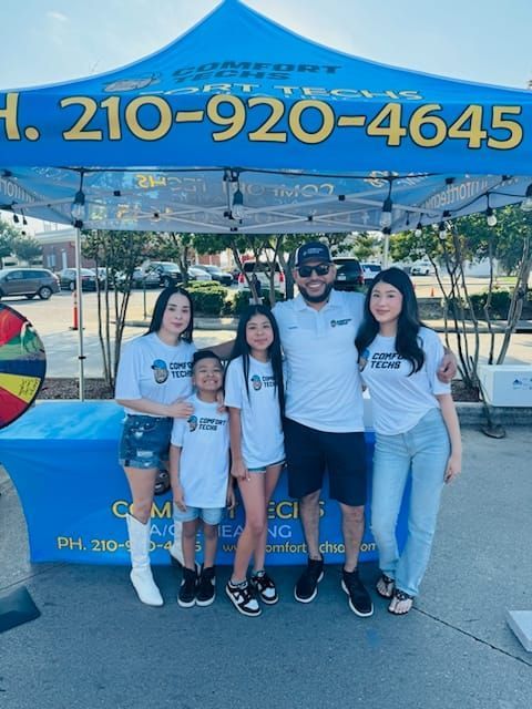 Family posing under a blue event tent at an outdoor festival, with a colorful prize wheel nearby.