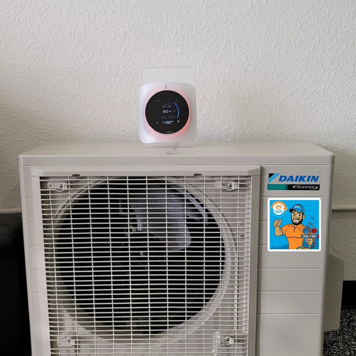 Outdoor air conditioner with a small round smart display on top, against a white wall.
