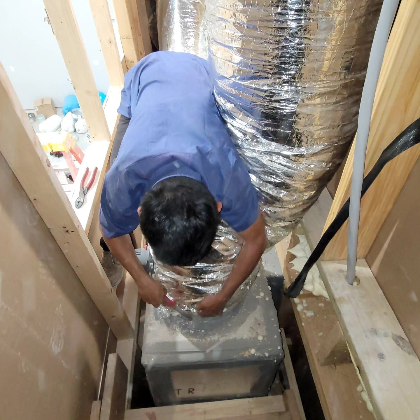 Person crouching in a narrow utility space, inspecting HVAC ducting and equipment.