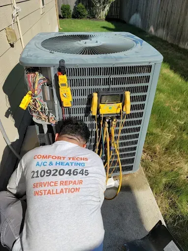 Technician servicing outdoor air conditioner unit with tools and gauges beside a house.