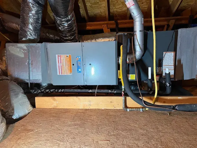 Person crouching in a narrow utility space, inspecting HVAC ducting and equipment.