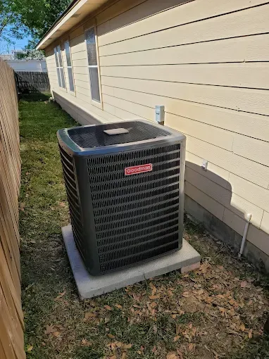 Outdoor HVAC unit beside a beige house with white-trimmed windows and a fence line.