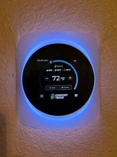 Smart thermostat with blue backlight on a textured wall, showing 72°F.