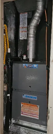 Furnace unit in a narrow utility closet with silver ductwork and metal panels.