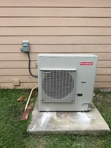 Outdoor air conditioner unit beside a beige house wall on a concrete pad, with grass and utility meter nearby